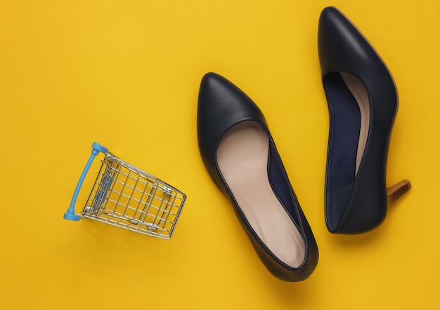 Minimalistic fashion and shopping concept Leather high heel shoes shopping trolley on yellow pastel background