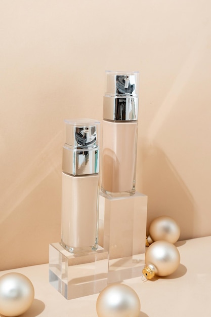 A minimalistic scene of foundation bottle on glass podium with christmas decorative balls on beige background