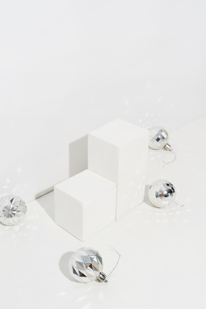 A minimalistic scene of a podium with christmas decorative balls and pine tree on light background