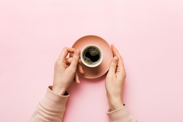 Minimalistic style woman hand holding a cup of coffee on Colored background Flat lay top view cappuccino cup Empty place for text copy space Coffee addiction Top view flat lay