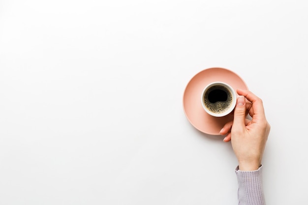 Minimalistic style woman hand holding a cup of coffee on Colored background Flat lay top view cappuccino cup Empty place for text copy space Coffee addiction Top view flat lay