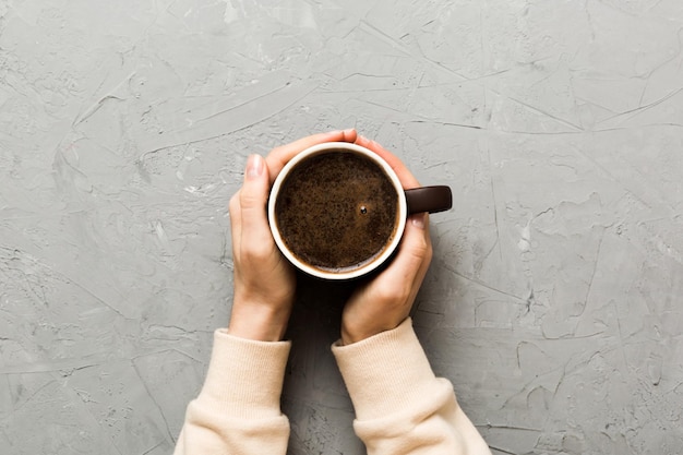 Minimalistic style woman hand holding a cup of coffee on Colored background Flat lay top view cappuccino cup Empty place for text copy space Coffee addiction Top view flat lay