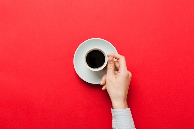 Minimalistic style woman hand holding a cup of coffee on Colored background Flat lay top view espresso cup Empty place for text copy space Coffee addiction Top view flat lay