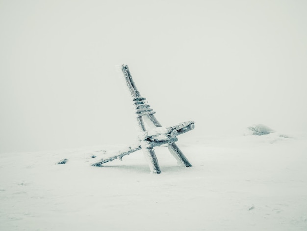 Minimalistic winter background with a frozen wooden chair with a frosty haze against the gray sky of the polar day Polar harsh comfort poor visibility