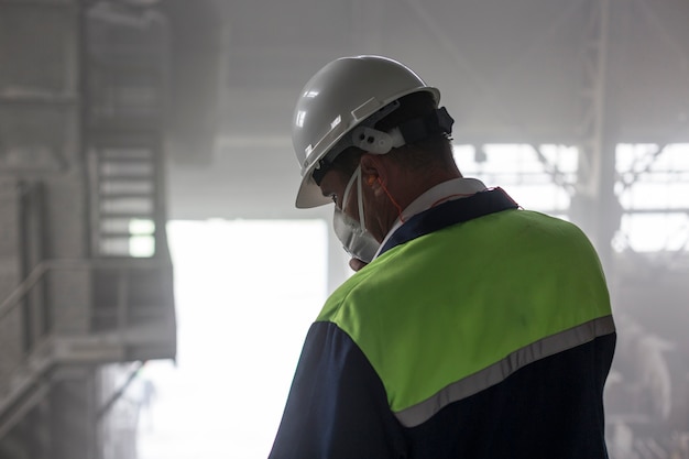 Mining engineer in white helmet and respirator inspects dusty dirty workshop