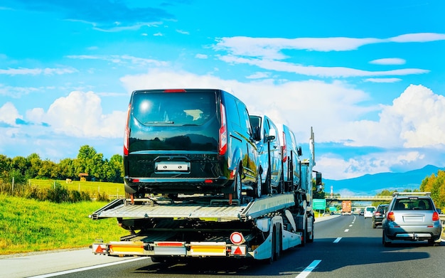 Minivans Car carrier transporter truck in road. Mini vans Auto vehicles hauler on driveway. European transport logistics at haulage work transportation. Heavy haul trailer with tow on highway.