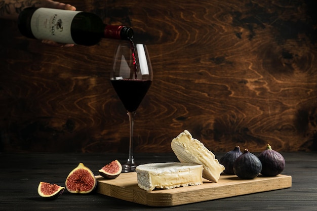 Minsk Belarus 02102022 Camembert cheese fresh figs on a wooden cutting board Pouring a glass of dry red wine from the bottle