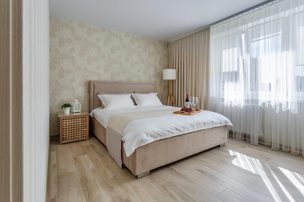 MINSK BELARUS MAY 2020 Double bed with pillows in interior of intimate bedroom in flat in light style apartments with still life decoration from two empty wine glasses