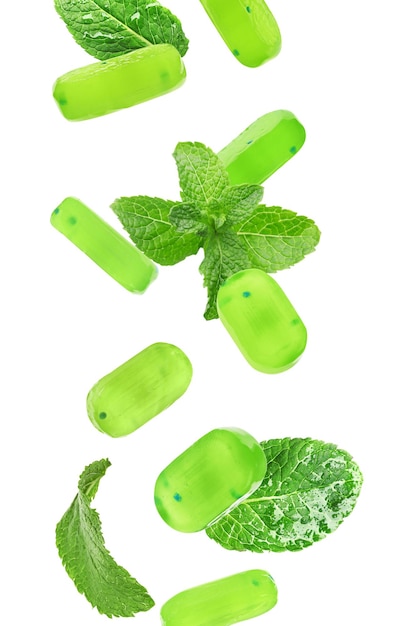 Mint hard candies and green leaves falling on white background