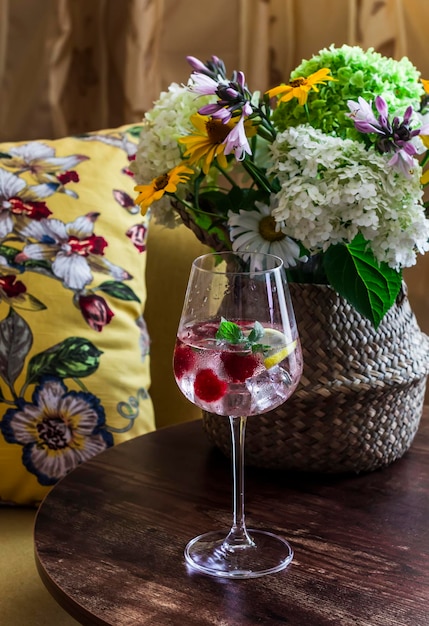 Photo mint raspberry lemon alcoholic cocktail on a wooden table with a basket of flowers near the sofa with bright pillows cozy interior concept