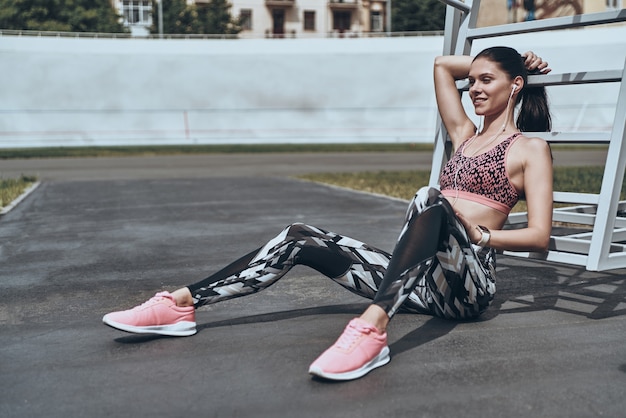 Minute to rest. Beautiful young woman in sports clothing smiling and looking away 