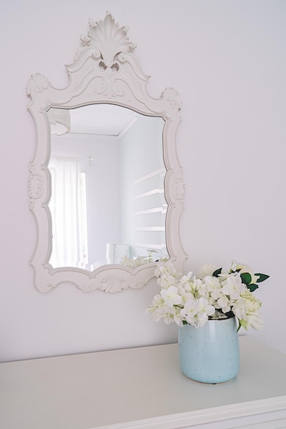 Mirror in carved wooden frame and vase with flowers in bright interior