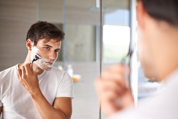 Mirror shaving and face of man in bathroom for facial grooming wellness and skincare at home Health skincare and serious male person shave beard for hygiene cleaning and hair removal with razor