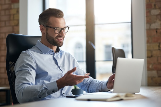 Mirthful employee looking at the laptop screen and smiling