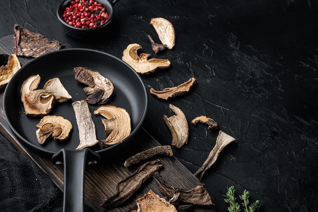 Mix of chopped wild dried mushrooms set in cast iron frying pan, on black table