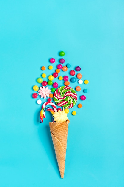 mix colorful chocolate sweets spilled out of ice cream waffle cone on blue  Flat lay