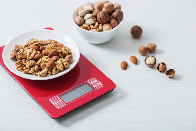 Mix of different nuts on  kitchen scale on a white table