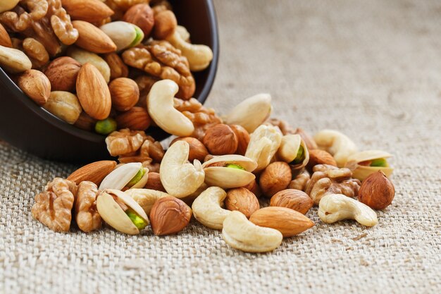 Mix of different nuts in a wooden cup against the background of fabric from burlap