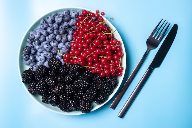 Mix of fresh berries blueberries blackberries and red currants in a plate against a blue background Fruit berry background