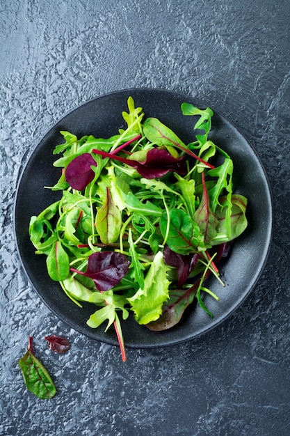 Mix fresh leaves of arugula, lettuce, spinach, beets for salad on a dark stone surface