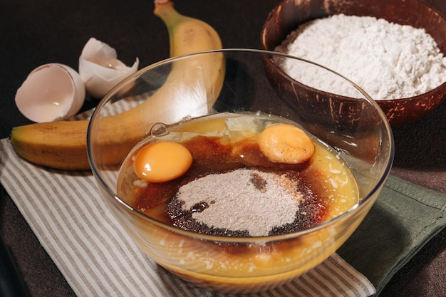 Mix of mashed banana, melted butter, cane sugar and egg for cooking banana bread on brown background