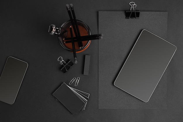 Mix of office supplies and business gadgets on a modern office desk. Black object on a black background.