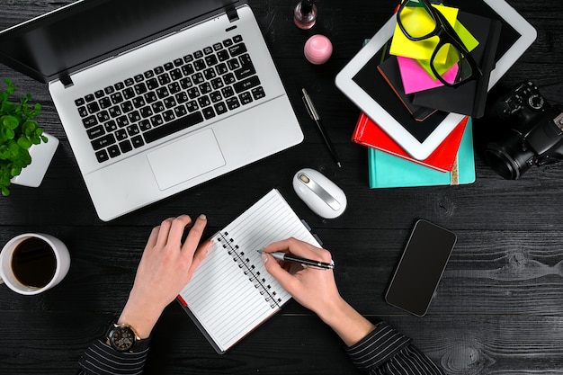 Mix of office supplies and gadgets on a wooden desk background view from above