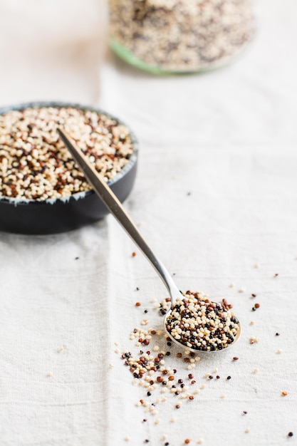 Mix of raw white red and black quinoa in a bowl and in a spoon on a cloth Healthy gluten free food Vertical view