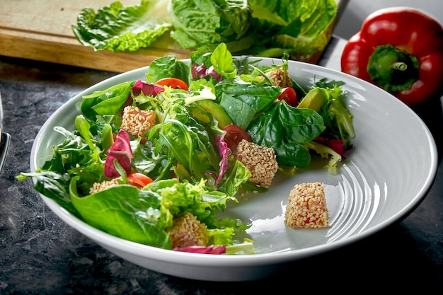 Mix salad with salmon, cherry tomatoes and avocado, served in a white plate on a dark marble table. Restaurant food.