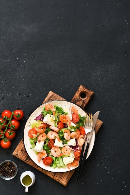 Mix salad with shrimp brie cheese and tomato sauce on a black concrete background top view