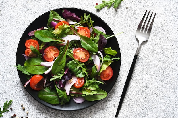 Mix salad with tomatoes, onions and olive oil in a black plate.