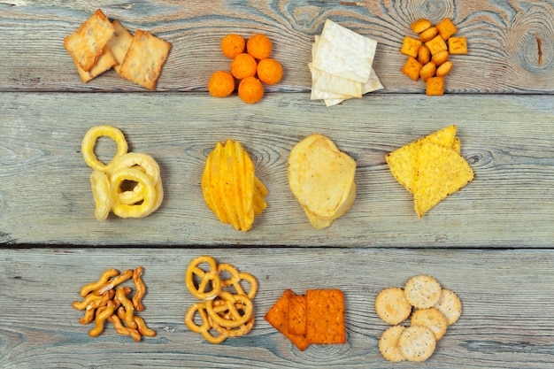 Photo mix of snacks : pretzels , crackers , chips and nachos on the table