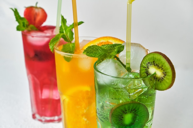 Mix of three bright colored delicious cold lemonade carafes of kiwi and orange and strawberry with mint on light surface