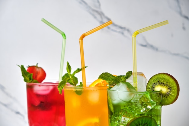 Mix of three bright colored delicious cold lemonade carafes of kiwi and orange and strawberry with mint on light surface