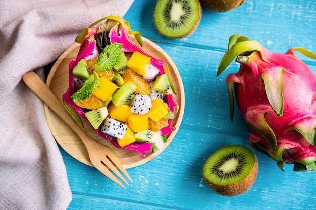 Mix tropical fruits salad served in half a dragon fruit on wooden table