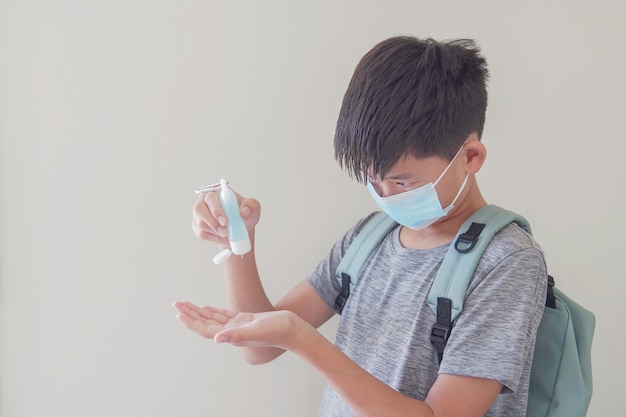 Mixed Asian preteen boy wearing mask and applying hand sanitizer, back to school concept