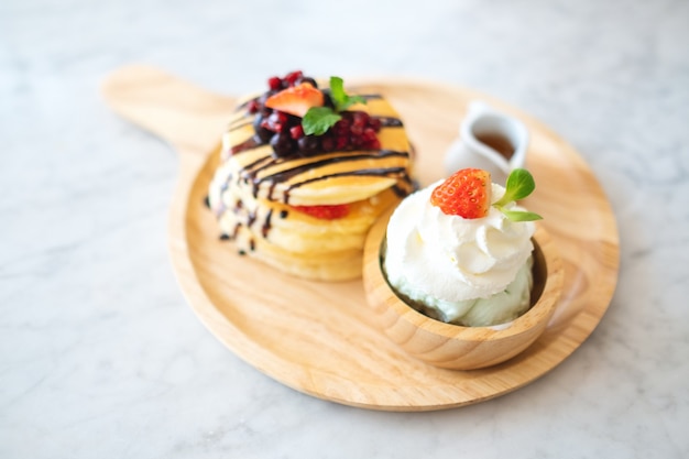 A mixed berries pancakes with ice cream and whipped cream in wooden plate