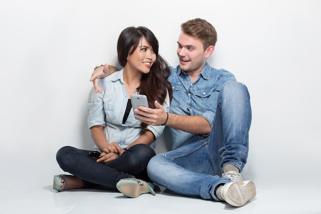 Mixed couple sitting on the floor while doing something with his smartphone