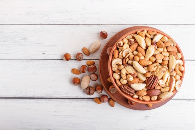 Mixed different kinds of nuts in ceramic bowl on white wooden background with copy space.