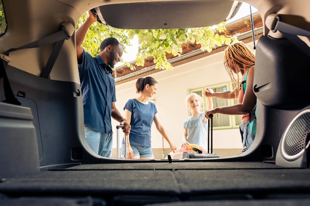 Mixed family and friends travelling on vacation with vehicle, going on summer holiday. Little girl with mother and young couple leaving with automobile on road trip journey, adventure.