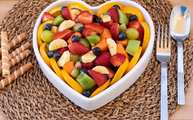 Mixed and fresh colorful fruit salad in a heart-shaped white ceramic plate. Wooden background