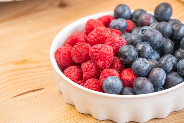 Mixed fresh fruits (strawberry, raspberry, blueberry, kiwi, mango) on wood bowl