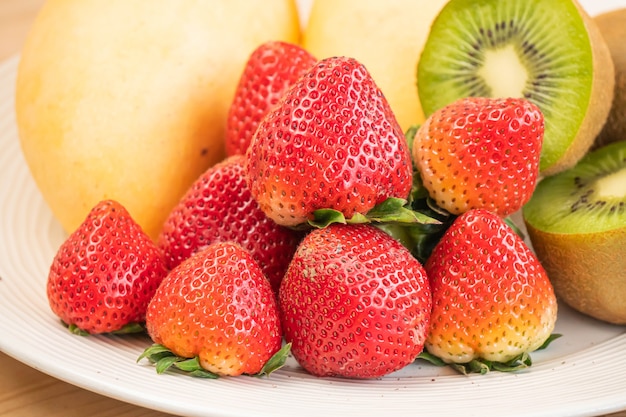 Mixed fresh fruits (strawberry, raspberry, blueberry, kiwi, mango) on wood bowl