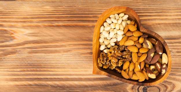 Mixed nuts in a bowl in the form of a heart on a brown wooden background