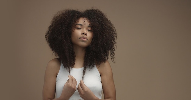 Mixed race black woman portrait with big afro hair curly hair in beige background Touching her hair