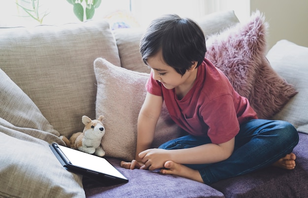 Mixed race kid sitting on sofa watching cartoons on tablet,Portrait 6-7 year old boy playing game on touch pad.