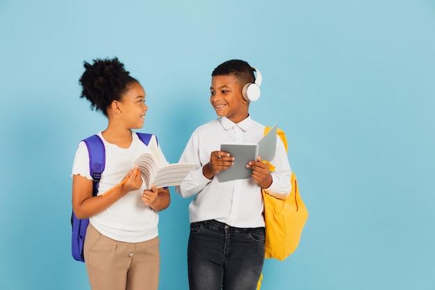 A mixed race schoolboy and an African American schoolgirl are reading an outline together in a school classroom on a blue background back to school concept