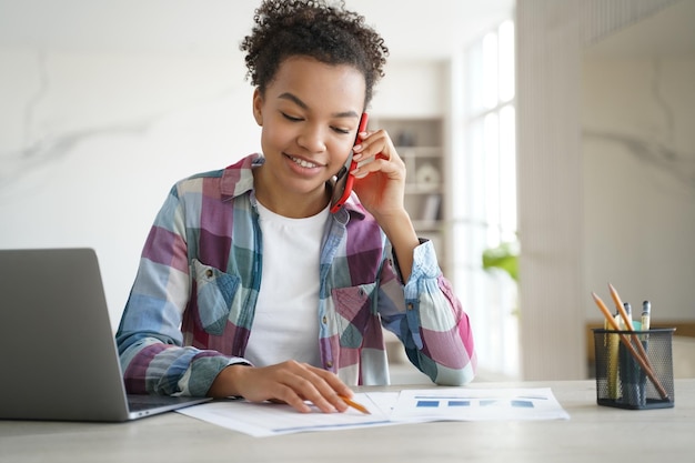 Mixed race teen girl school student call by phone discussing homework with friend sitting at desk