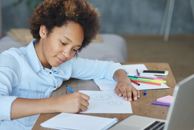 Mixed race teen schoolgirl looking focused while drawing on paper with colorful markers spending