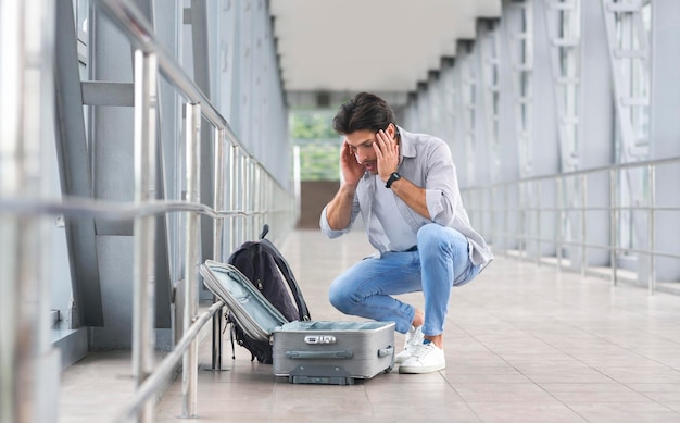 Mixed Up Luggage Desperate man sitting near airport terminal with suitcase